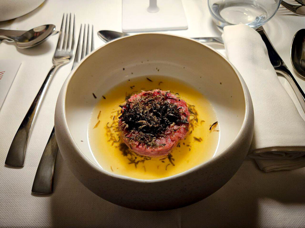 Un'immagine di presentazione di un piatto di alta cucina, una tartara in brodo cosparsa di scaglie di tartufo